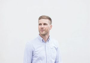 Mies seisoo vaaleansininen kauluspaita päällänsä. Tutkija Otto Tähkäpään valokuva.